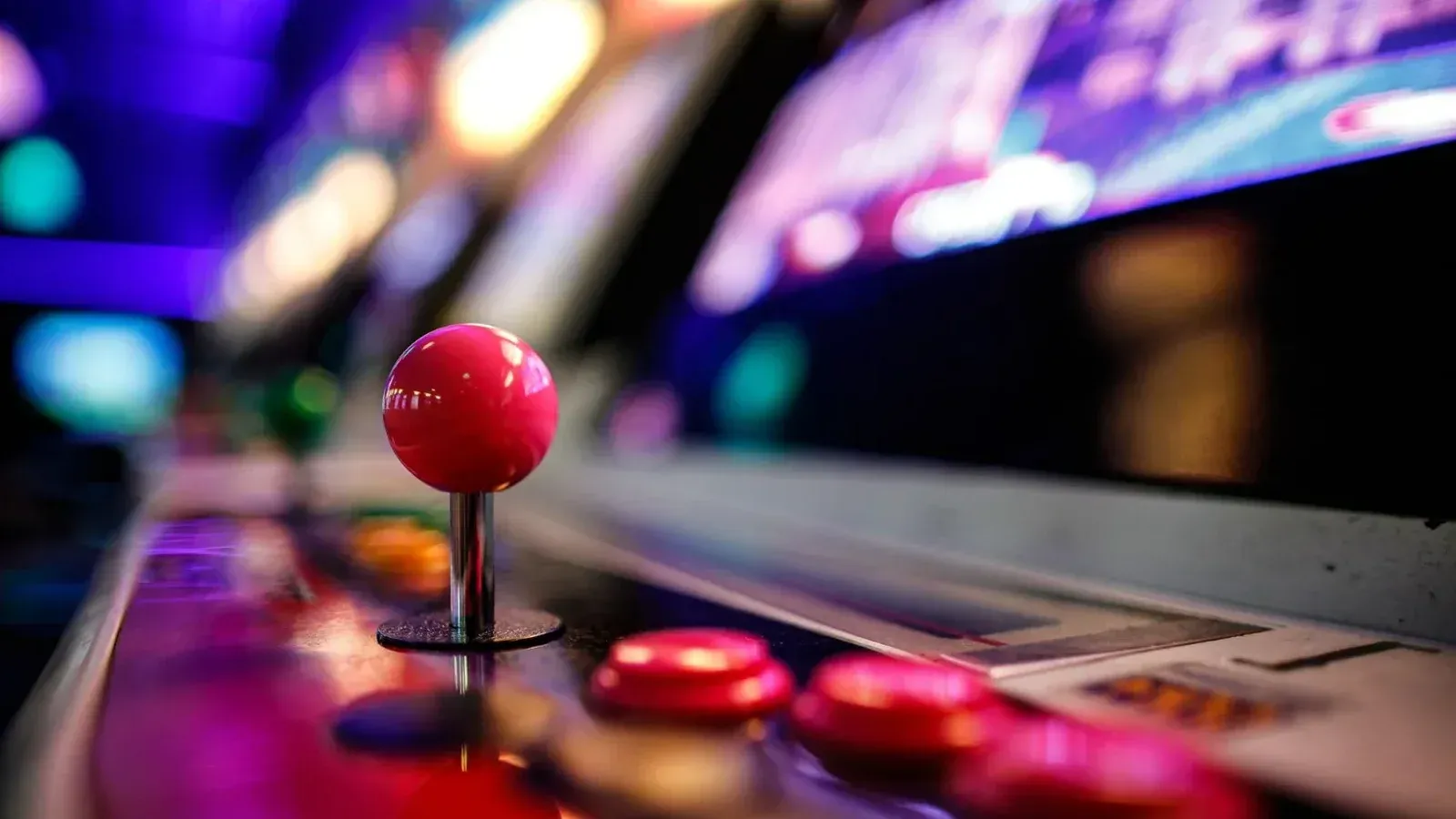 Close-up de un vibrante joystick de arcade retro y botones con luces borrosas en el fondo.