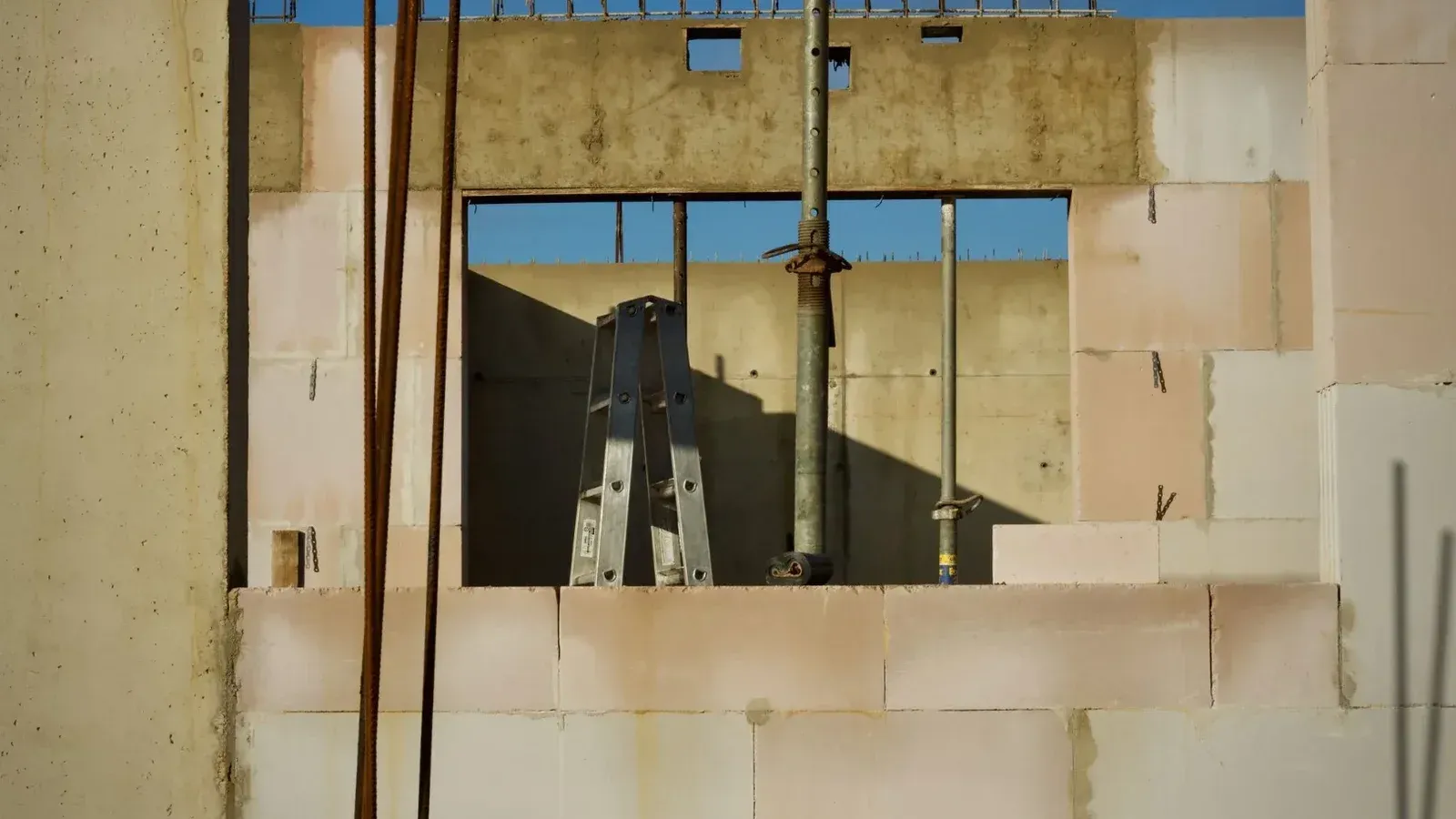 Vista de un sitio de construcción con paredes de hormigón y escalera de metal bajo un cielo azul.