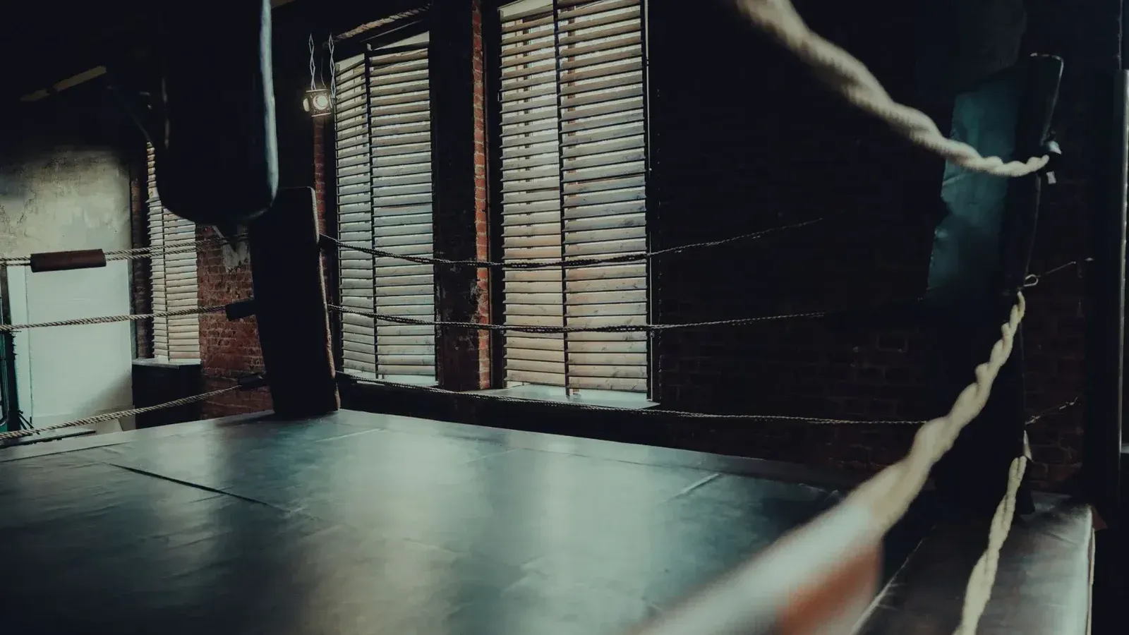 Anillo de boxeo vacío en un gimnasio atmosférico con iluminación de mal humor y paredes de ladrillo.
