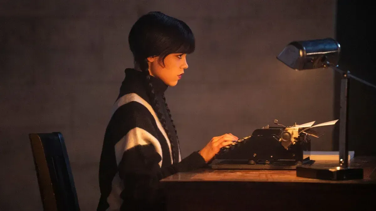 Jenna Ortega mientras el miércoles Addams se sienta en un escritorio con una máquina de escribir.