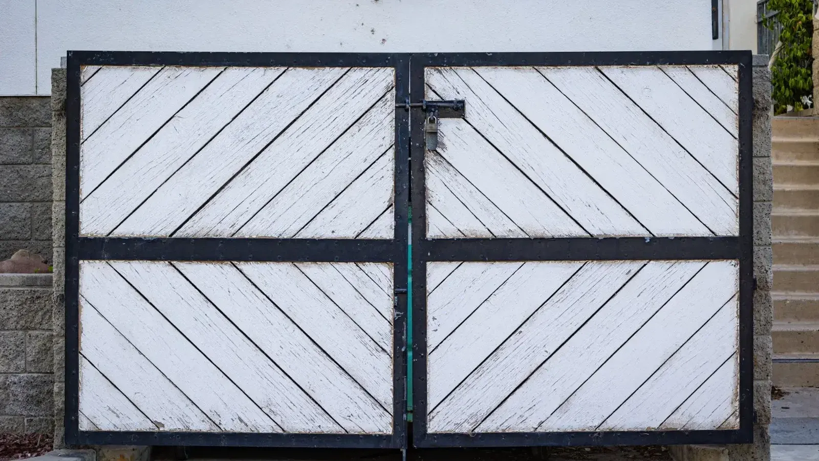 Una puerta de madera blanca rústica con paneles diagonales y un marco de metal negro en una entrada residencial.