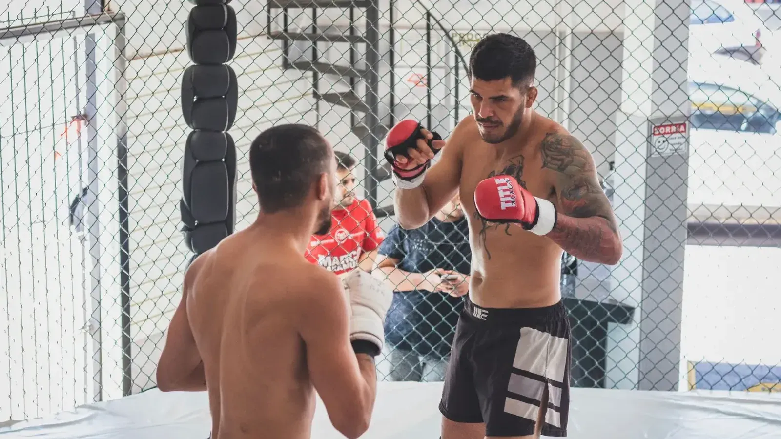 Dos luchadores masculinos entrenando en un gimnasio de jaula interior de MMA, mostrando habilidades de artes marciales.