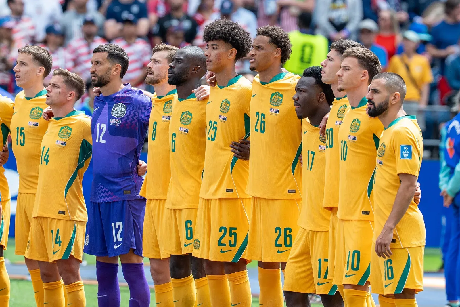 Jugadores de la selección de Australia, con uniforme amarillo, y su portero, de morado, formados y abrazados en fila sobre la cancha frente a la tribuna