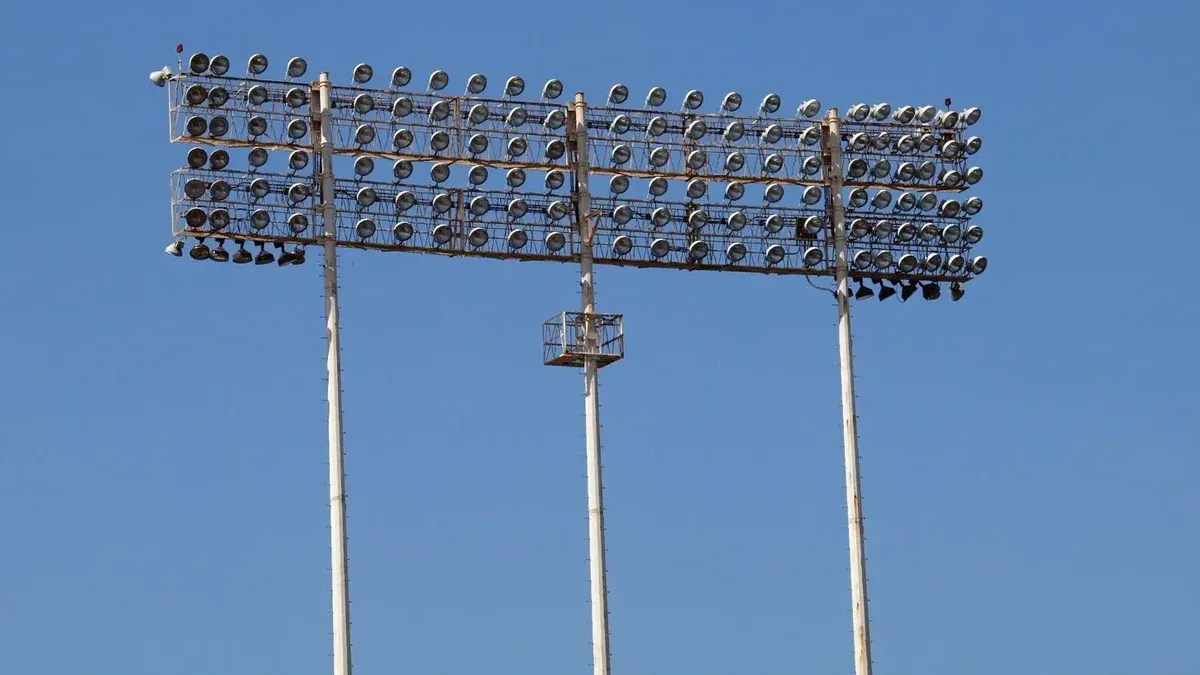 Tall stadium floodlights towering against a clear blue sky, perfect for outdoor sports lighting visuals.