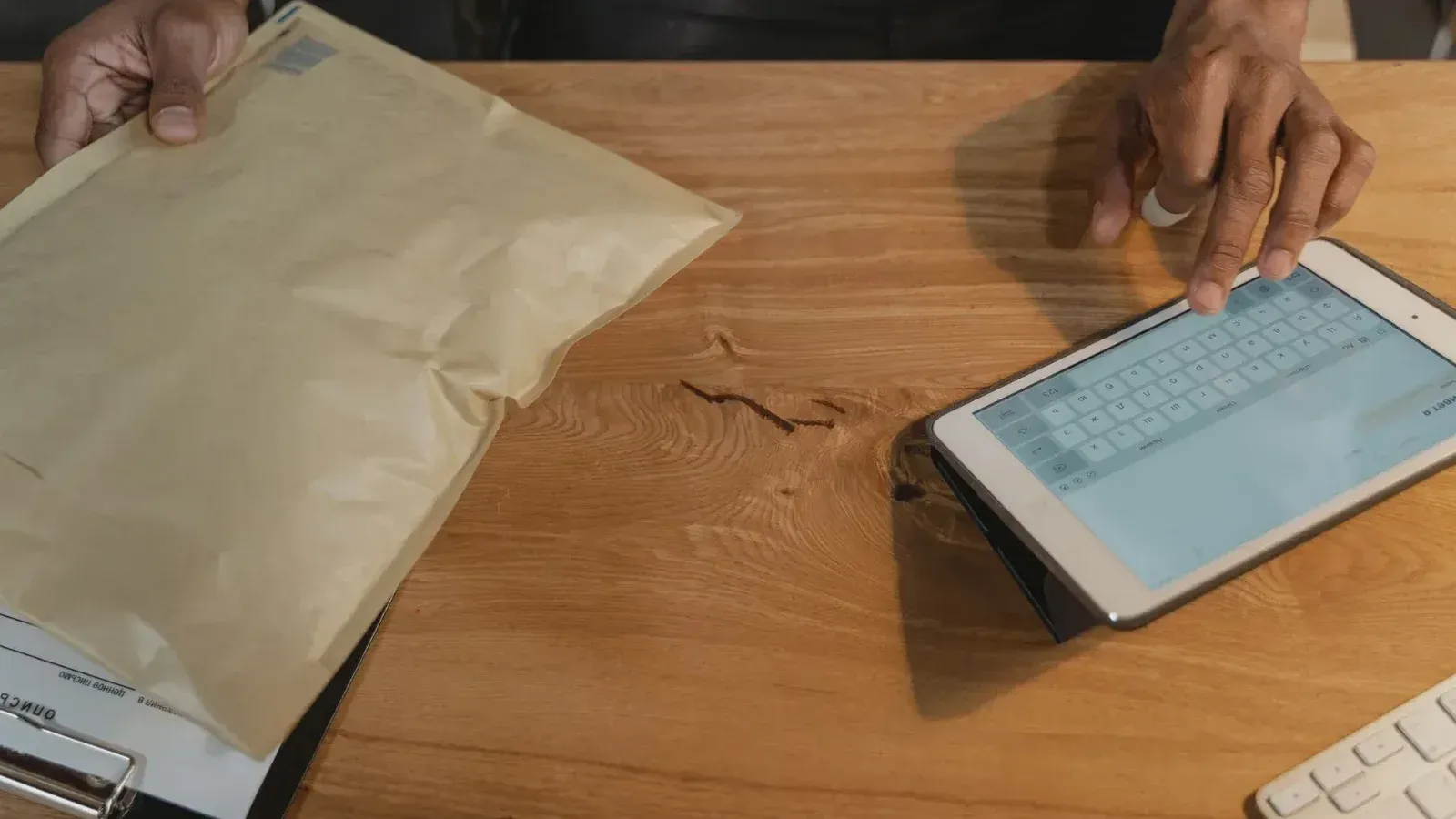 Persona que maneja la logística en una tableta con un paquete en una mesa de madera.