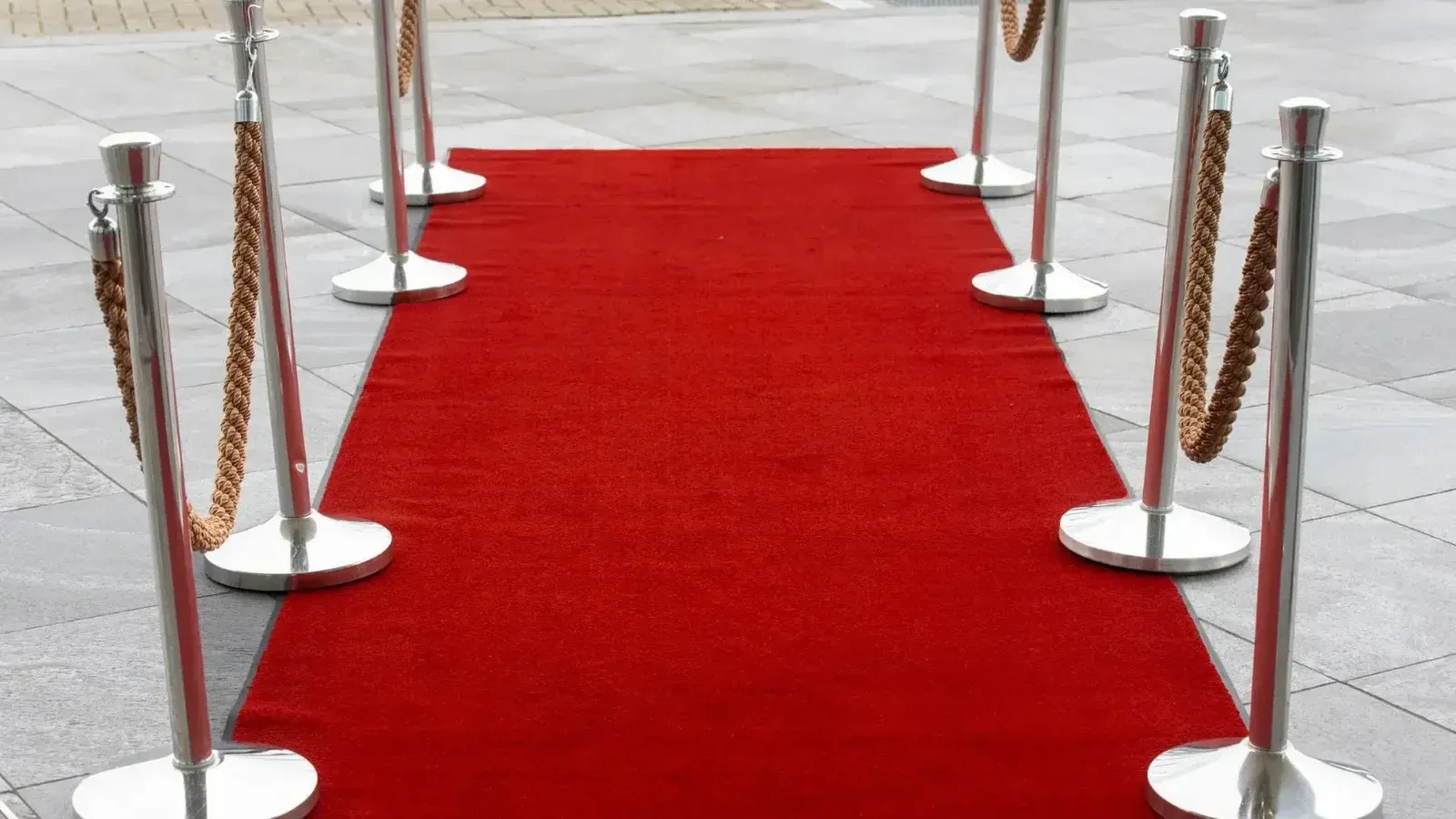 Entrada de alfombra roja con puntales en una superficie de azulejos, perfecta para eventos.