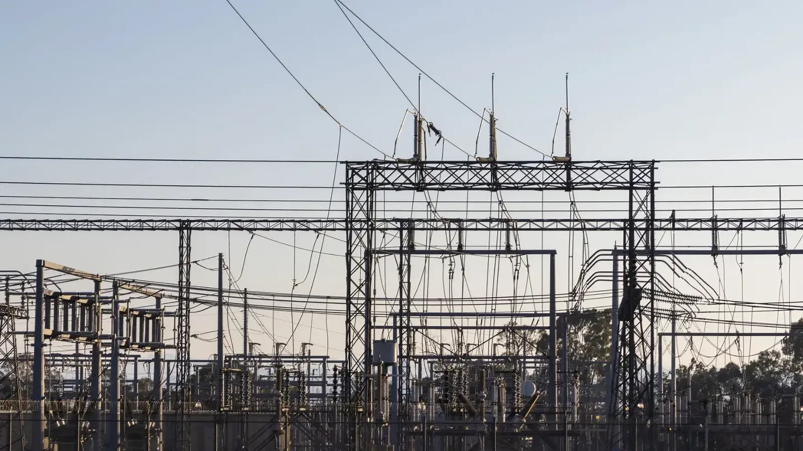 High-voltage electrical substation with steel structures and power lines at dawn.