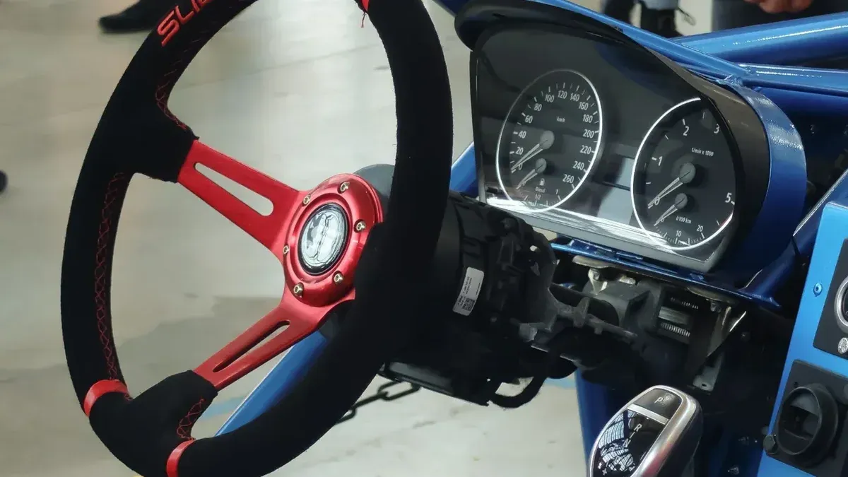 Close-up view of a custom racing steering wheel with red accents, featuring a dashboard and speedometer in a racing setting.