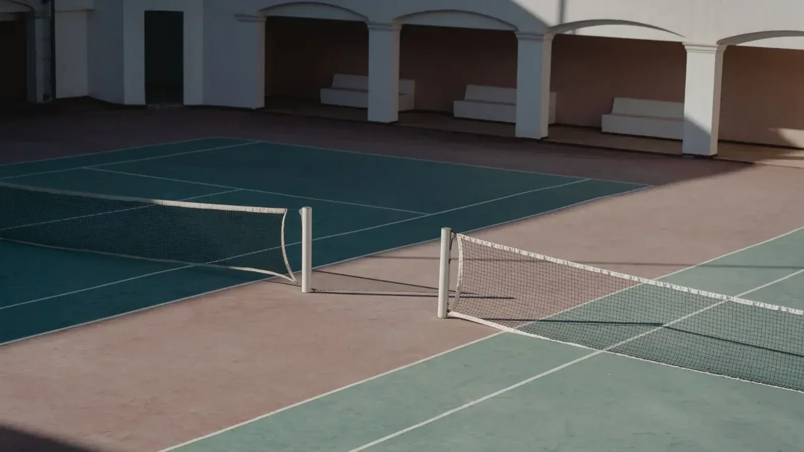 A deserted tennis court with shadows casting over the net, creating a serene atmosphere.