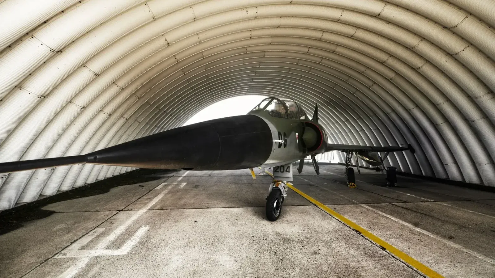 Un avión de combate estacionado dentro de un hangar militar arqueado, mostrando su elegante diseño.