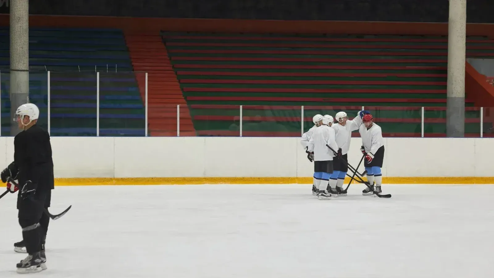 Group of athletes practicing ice hockey on an indoor rink with sticks and helmets.