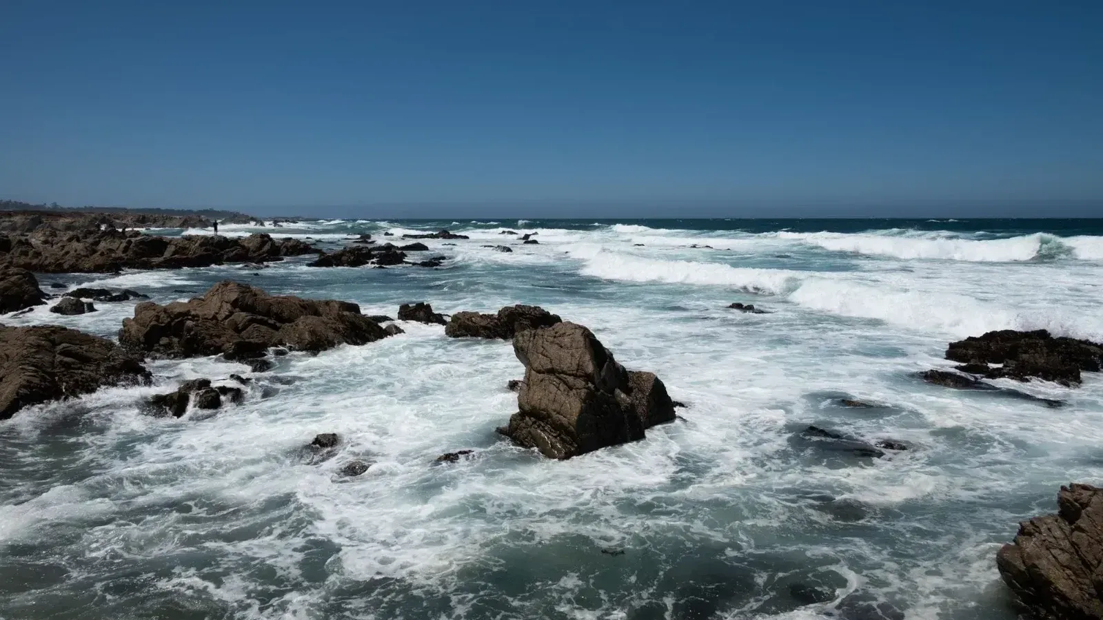 Impresionante costa de California con olas rompientes y rocas escarpadas bajo cielos azules despejados.