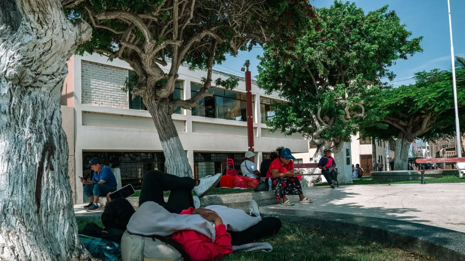 Una escena sincera de gente relajándose a la sombra de un parque en Pacasmayo, Perú, capturando la vida cotidiana.