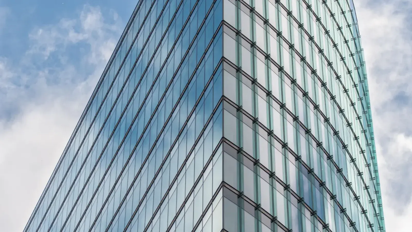 A sleek glass skyscraper reflecting the blue sky and clouds, showcasing modern architectural design.