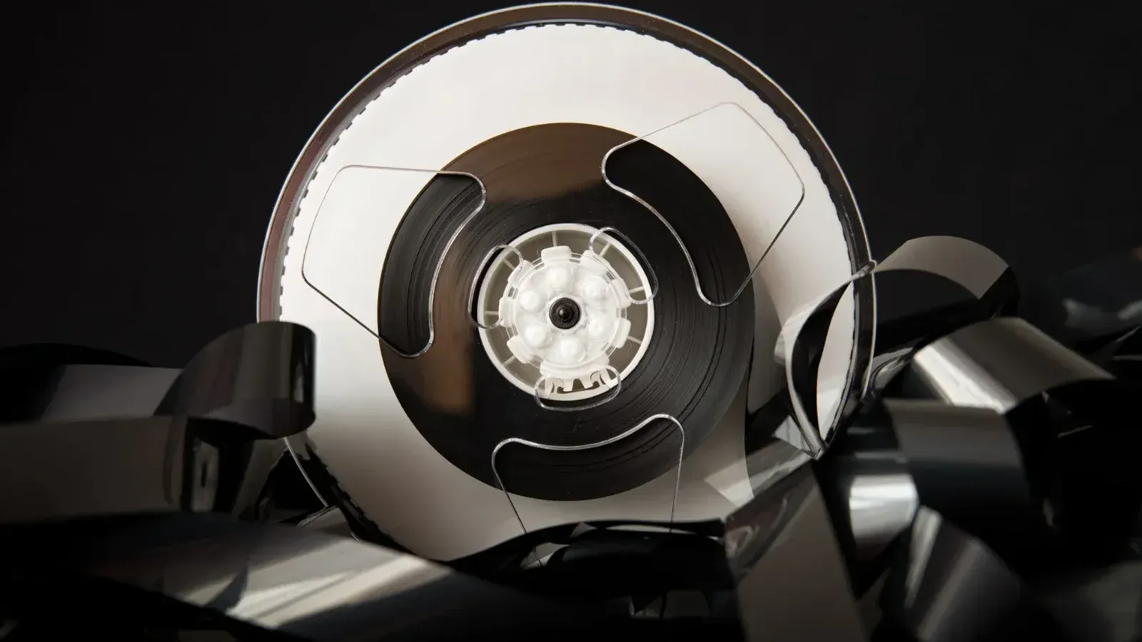 Vintage plastic bobbin with unrolled film for cinematography industry placed on black background