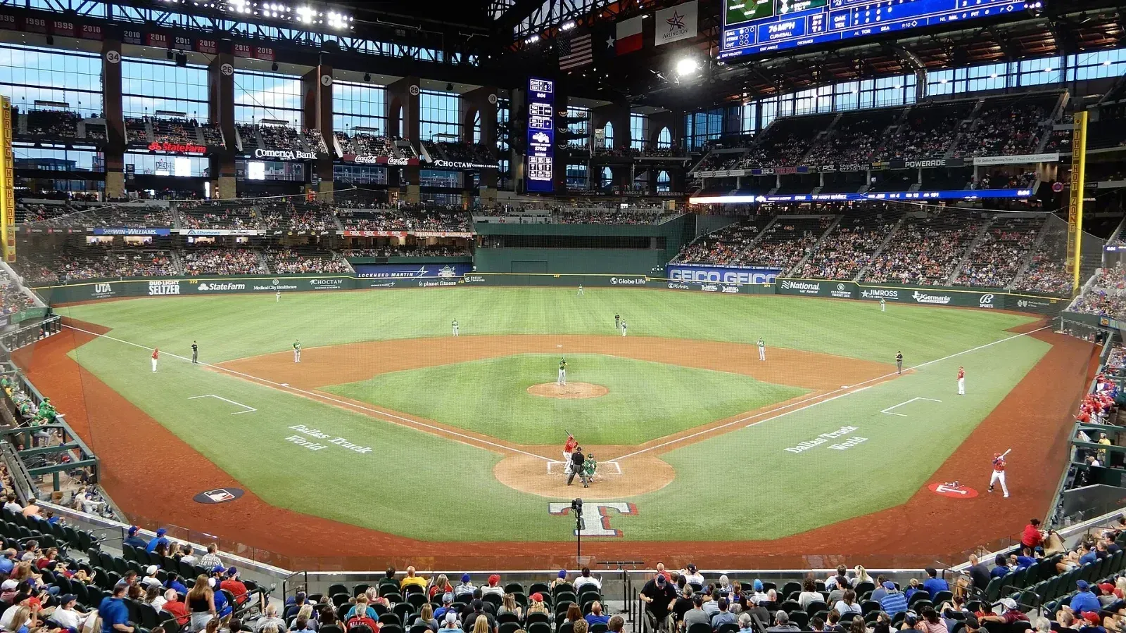 Vista general del interior de Globe Life Field durante un juego de béisbol, con el diamante, jugadores en el campo y gradas con público bajo el techo cerrado.