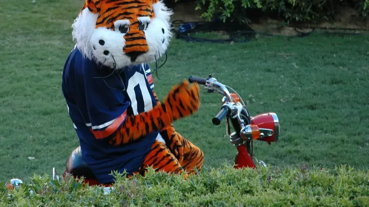 Descripción: Aubie, la mascota disfrazada de la Universidad de Auburn, entretiene a las multitudes en su bicicleta.