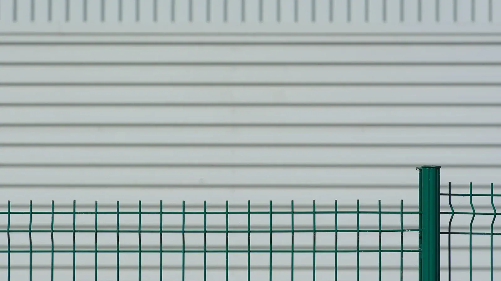 Valla de metal verde contrasta con una pared ondulada blanca, creando un patrón minimalista.