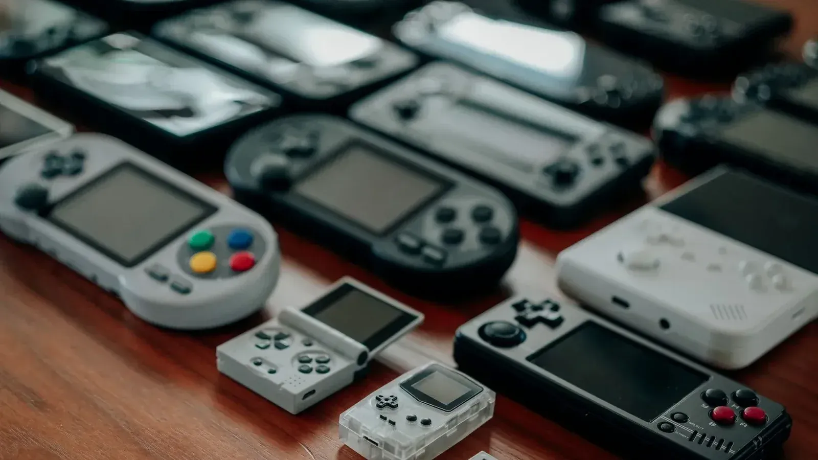 Colección de diversas consolas de juegos de mano retro sobre una superficie de madera, mostrando diseños clásicos y nostalgia.