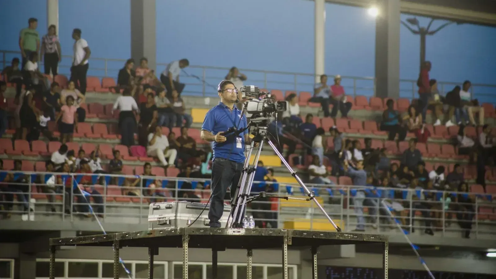 Camarógrafo en la plataforma capturando imágenes en un evento de estadio lleno de gente.