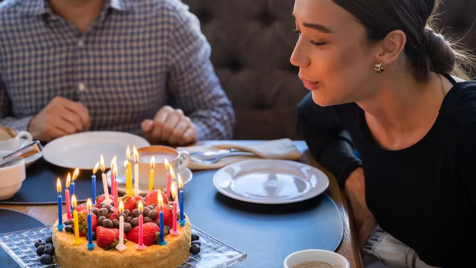 Una mujer soplando con alegría las velas en un pastel de cumpleaños con tapa de frutas, compartiendo un momento festivo.