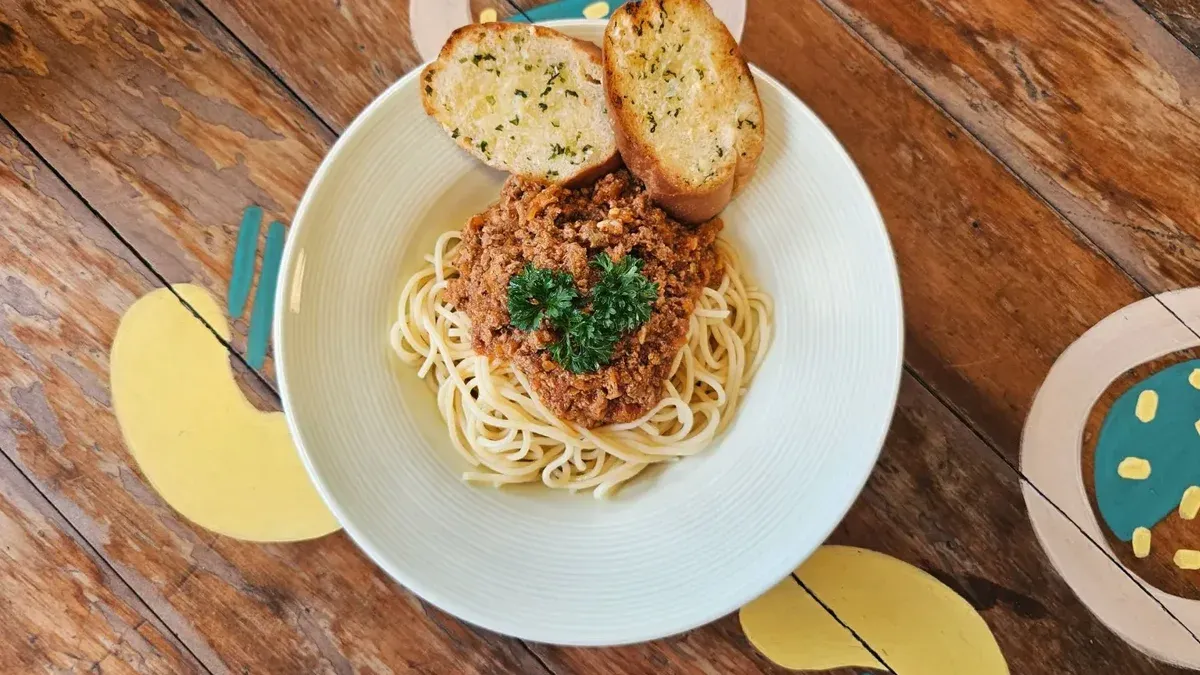 Close-up of spaghetti bolognese with garlic bread on a rustic table.