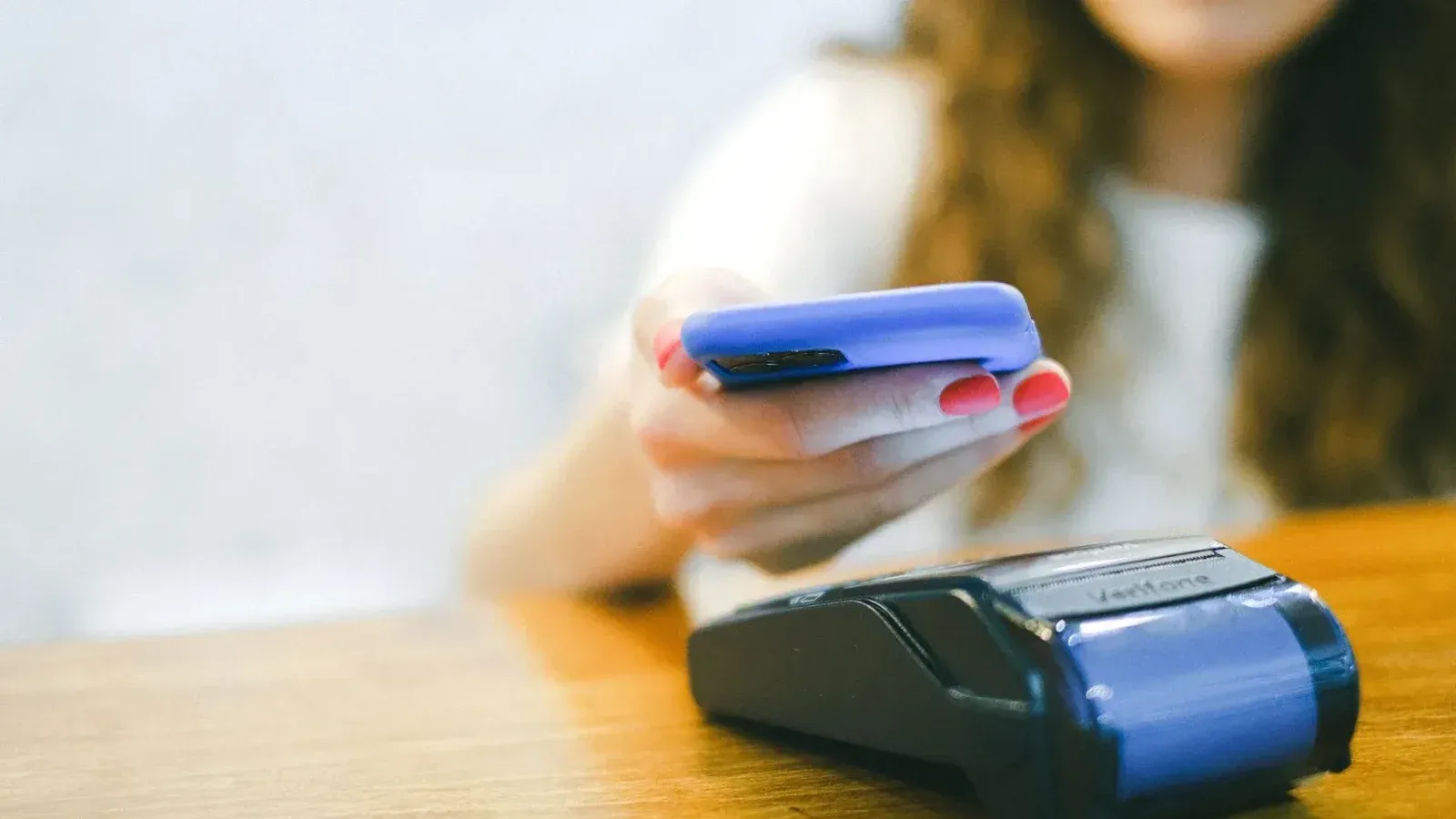 Close-up de una mujer haciendo un pago sin contacto usando un smartphone sobre un lector de tarjetas