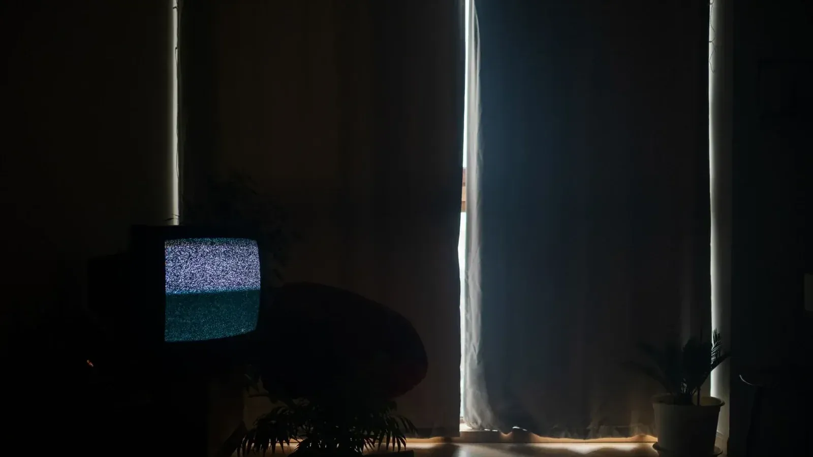 Una sala de estar con poca luz con estática en la televisión y cortinas hechas, creando una atmósfera de mal humor.