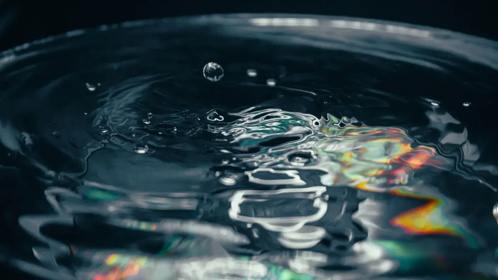 Close-up of a water droplet causing ripples with colorful prism reflection, captured in detail.
