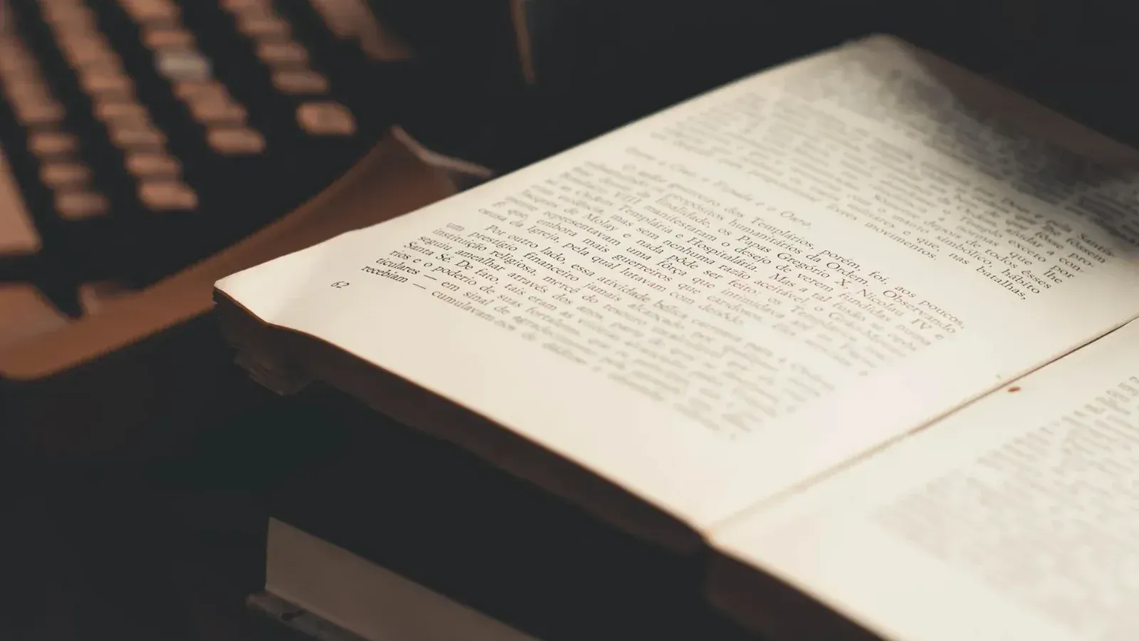 An open book with visible text in front of an antique typewriter, evoking a vintage literary theme.