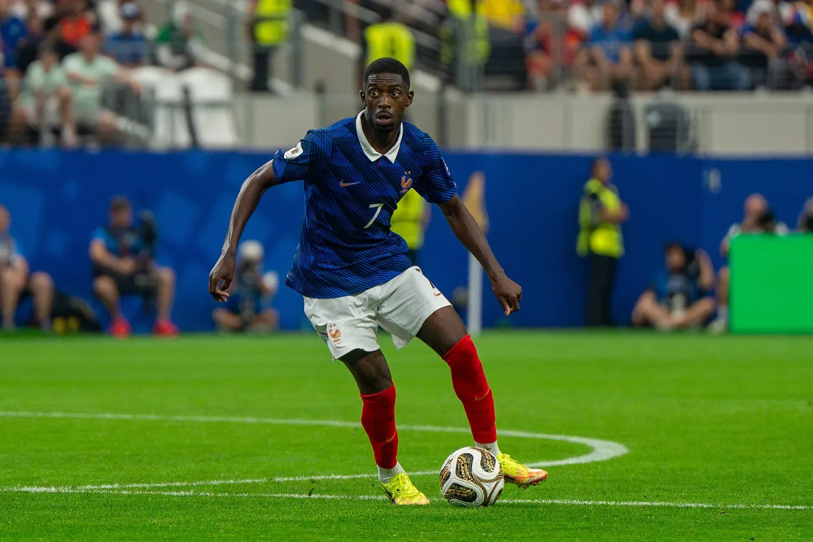 Ousmane Dembélé, con la camiseta azul número 7 de Francia, conduce el balón sobre el césped durante un partido.