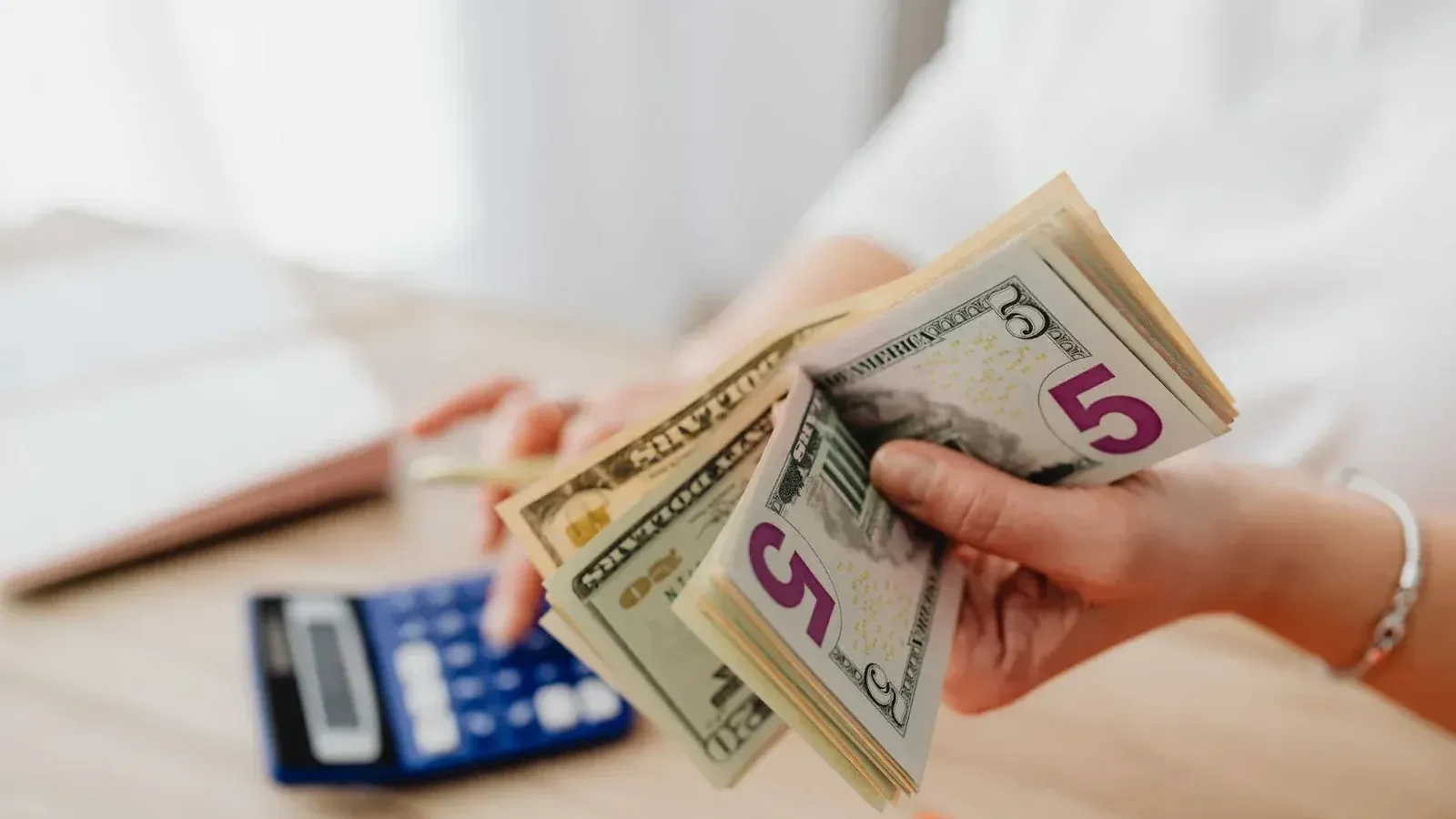 Close-up de manos contando billetes de dólar estadounidense con una calculadora, destacando las finanzas y los ahorros.