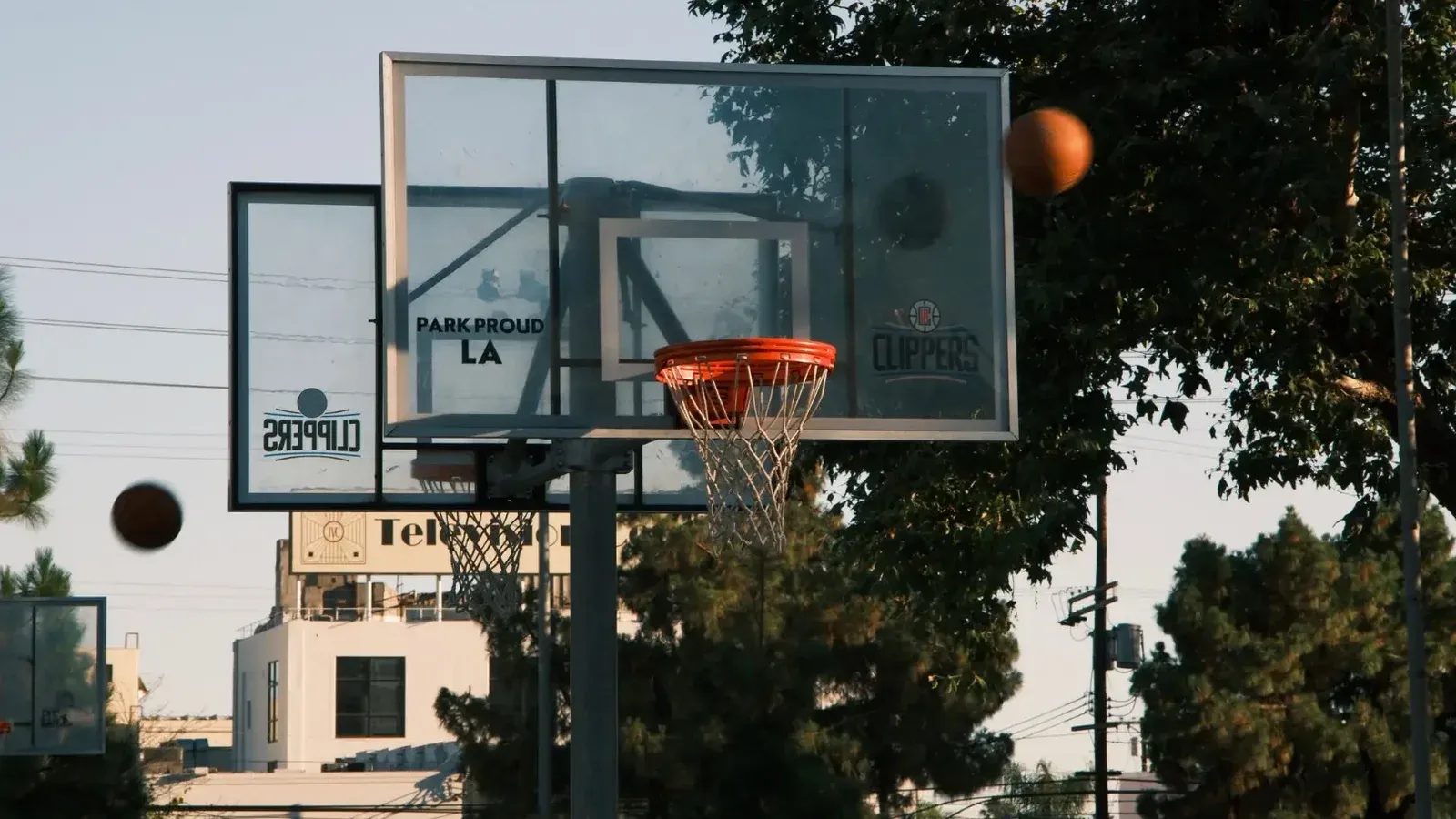 A basketball hoop on an outdoor court in Los Angeles, with trees and buildings in the background.