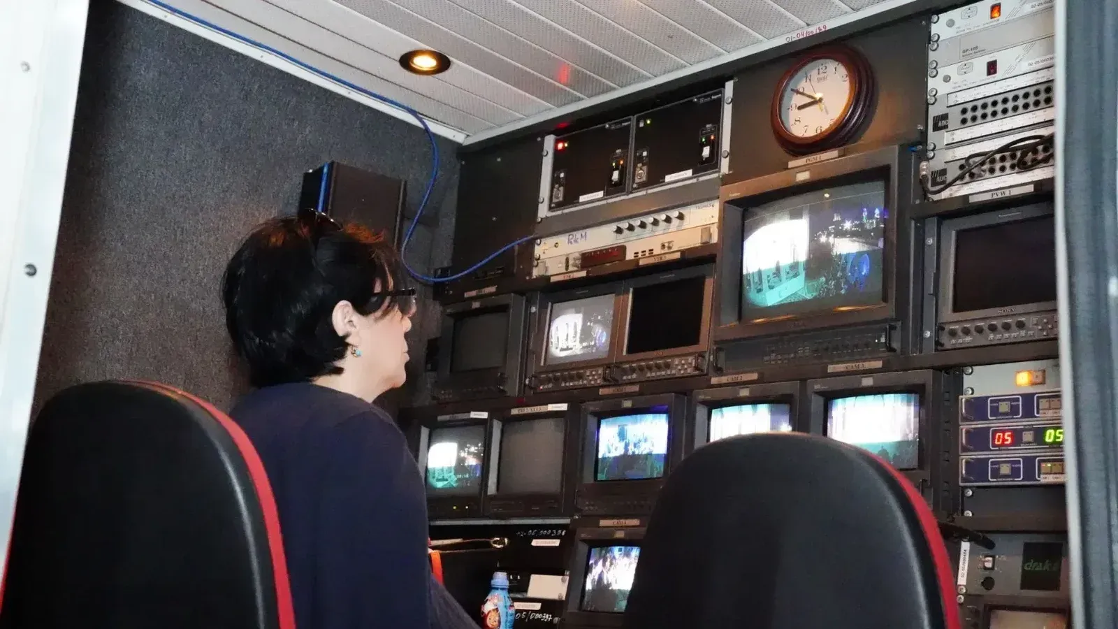 A professional in a TV broadcast control room with multiple screens and equipment.