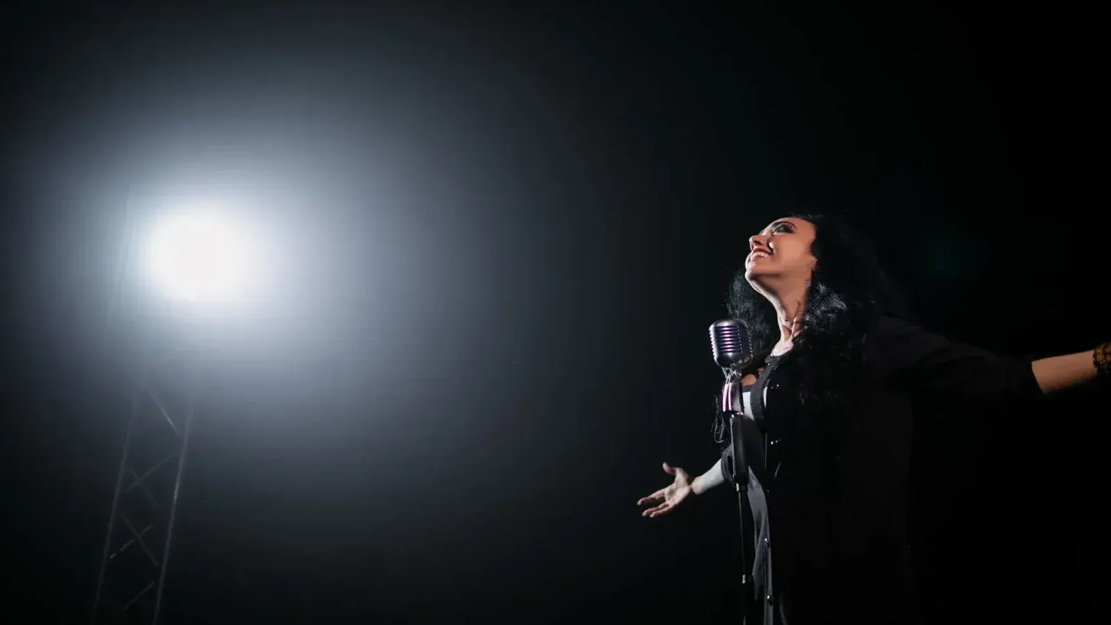 Una apasionada cantante femenina actúa en el escenario bajo un foco dramático.