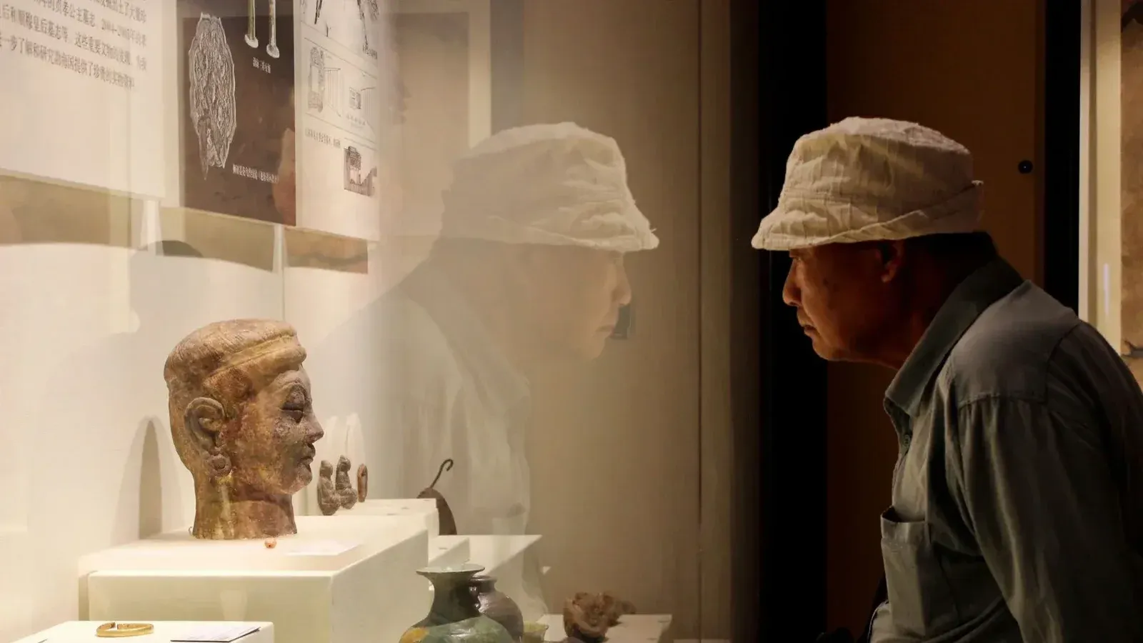Adult male observes ancient artifact display in a museum, reflecting history and learning.