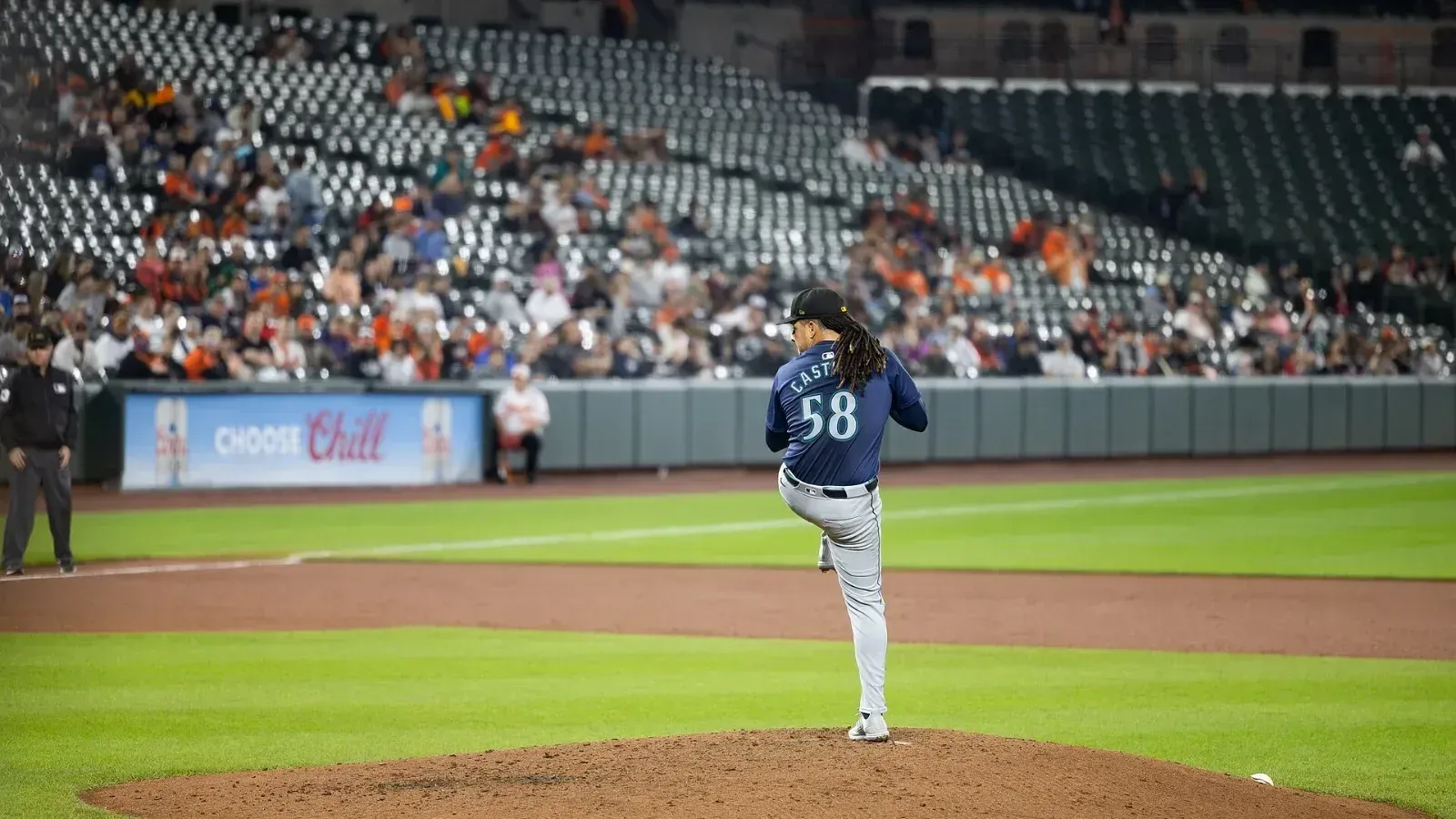Un lanzador con el número 58 en la camiseta levanta la pierna para lanzar desde el montículo, con aficionados en las gradas de un estadio de béisbol.
