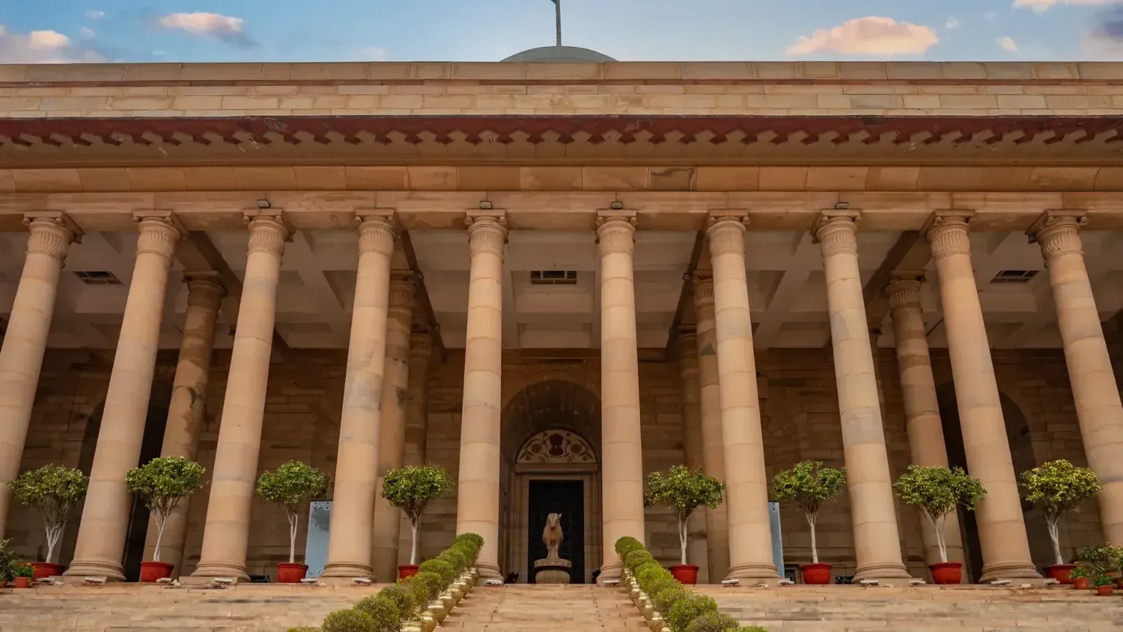 Edificio gubernamental en Nueva Delhi con columnas y una bandera india bajo un cielo vibrante.
