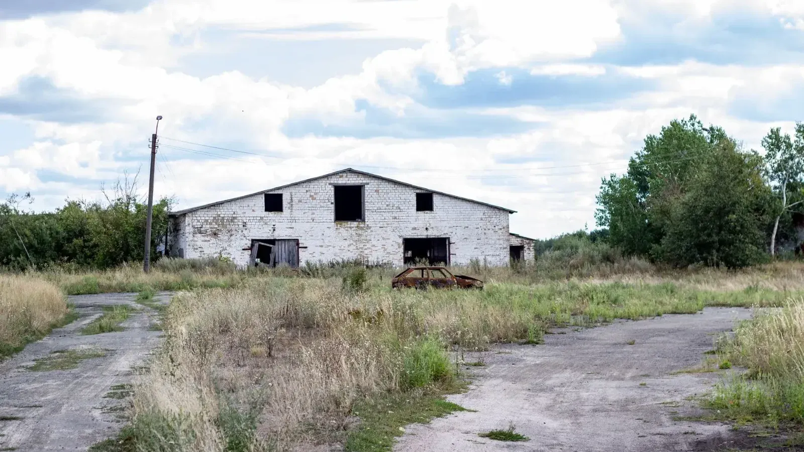 Antiguo almacén abandonado en una zona rural con césped cubierto y cielos nublados.