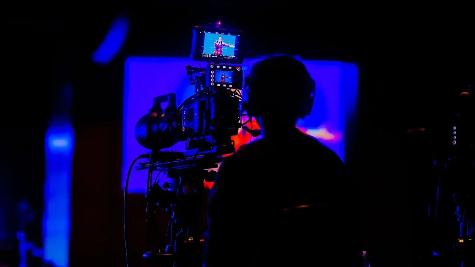 Camarógrafo capturando imágenes con poca luz durante el evento nocturno con colores vivos.
