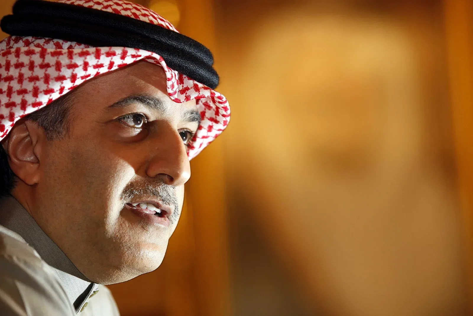 Salman bin Ibrahim Al Khalifa, con tocado a cuadros rojos y blancos y agal negro, habla de perfil frente a un fondo cálido desenfocado.