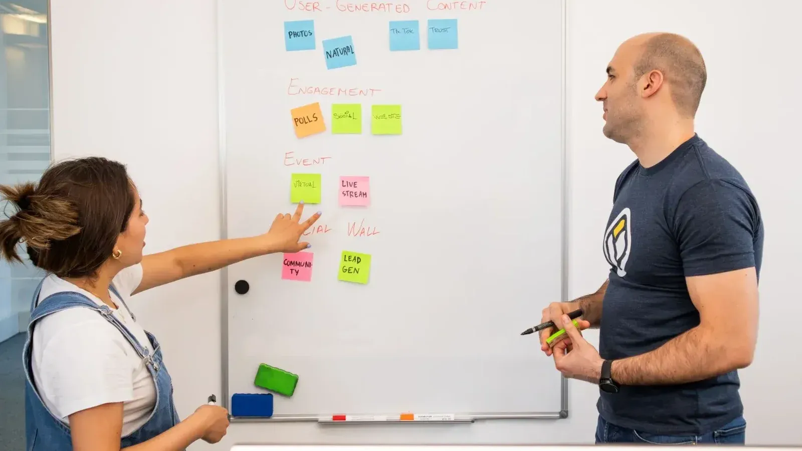 Dos profesionales que hacen una lluvia de ideas y planean proyectos en una pizarra en un entorno de oficina colaborativo.