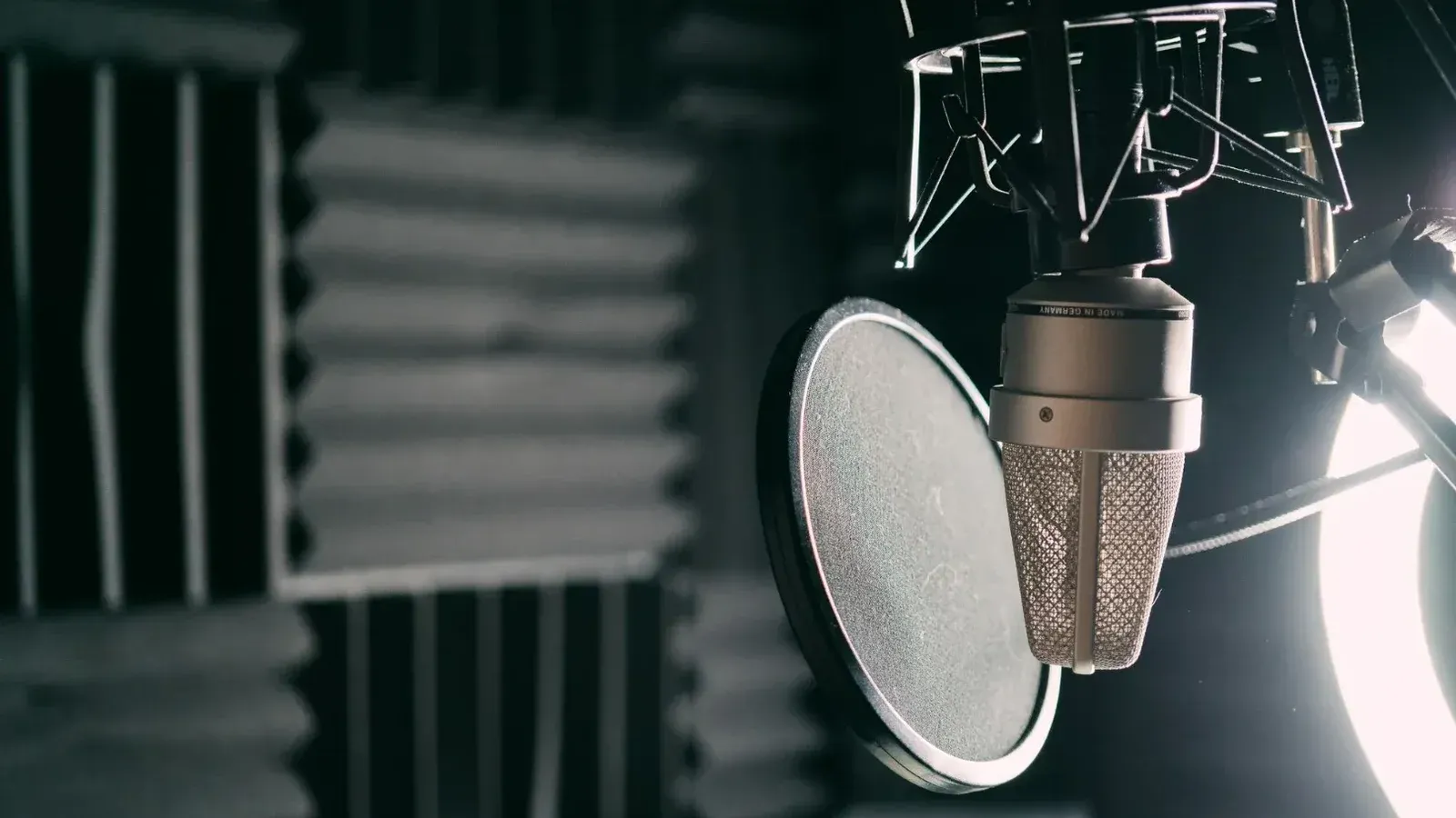 Primer plano de un micrófono de condensador con filtro pop en un estudio de sonido profesional.