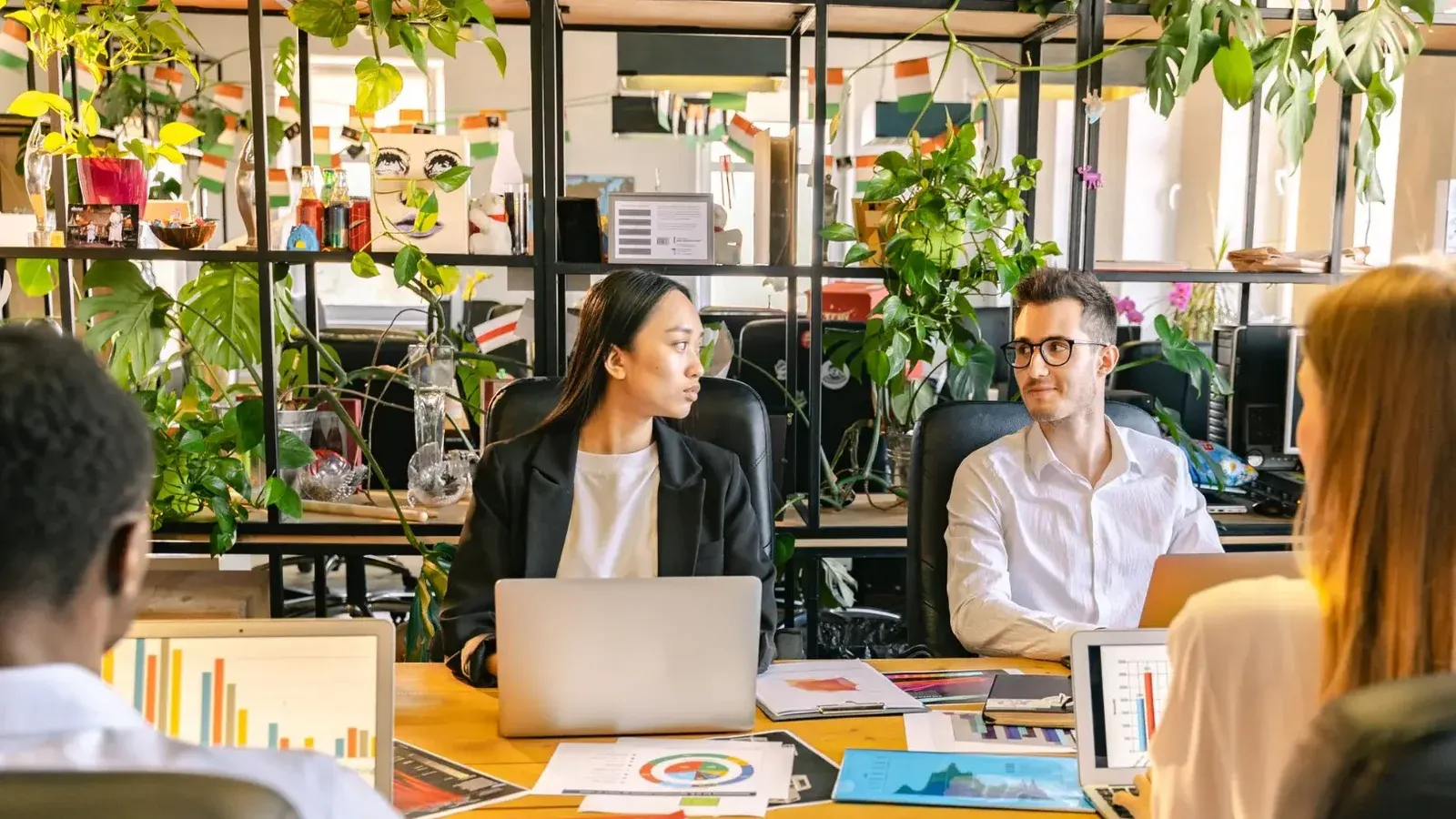 Un equipo diverso de profesionales discutiendo proyectos en un entorno de oficina lleno de plantas.