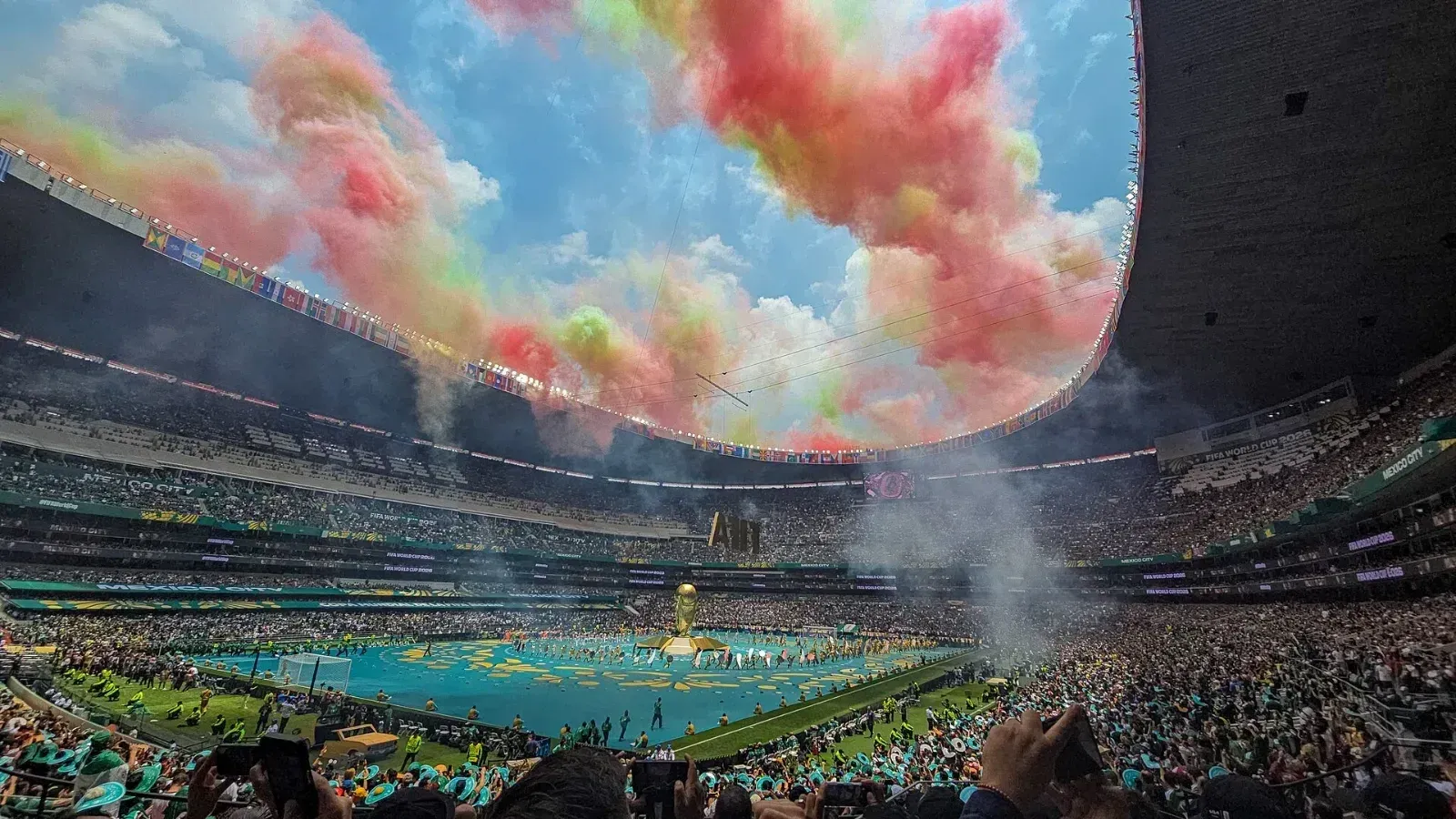 Estadio Azteca lleno durante la ceremonia inaugural del Mundial 2026, con humo verde, blanco y rojo en el cielo y un escenario azul sobre la cancha.
