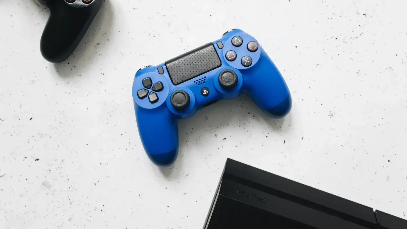 Una vista de cerca de los controladores de juego negros y azules sobre una superficie moteada blanca.