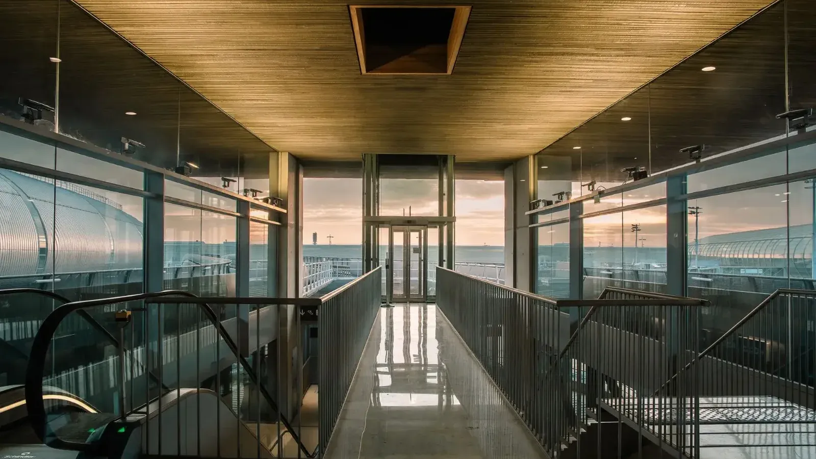 Un moderno corredor terminal del aeropuerto con paredes de vidrio, con vistas a la zona al aire libre al amanecer.