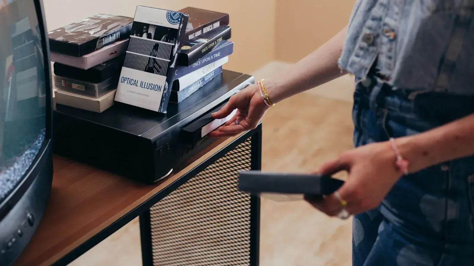 Una persona que configura una videograbadora con cintas VHS en un ambiente interior acogedor.