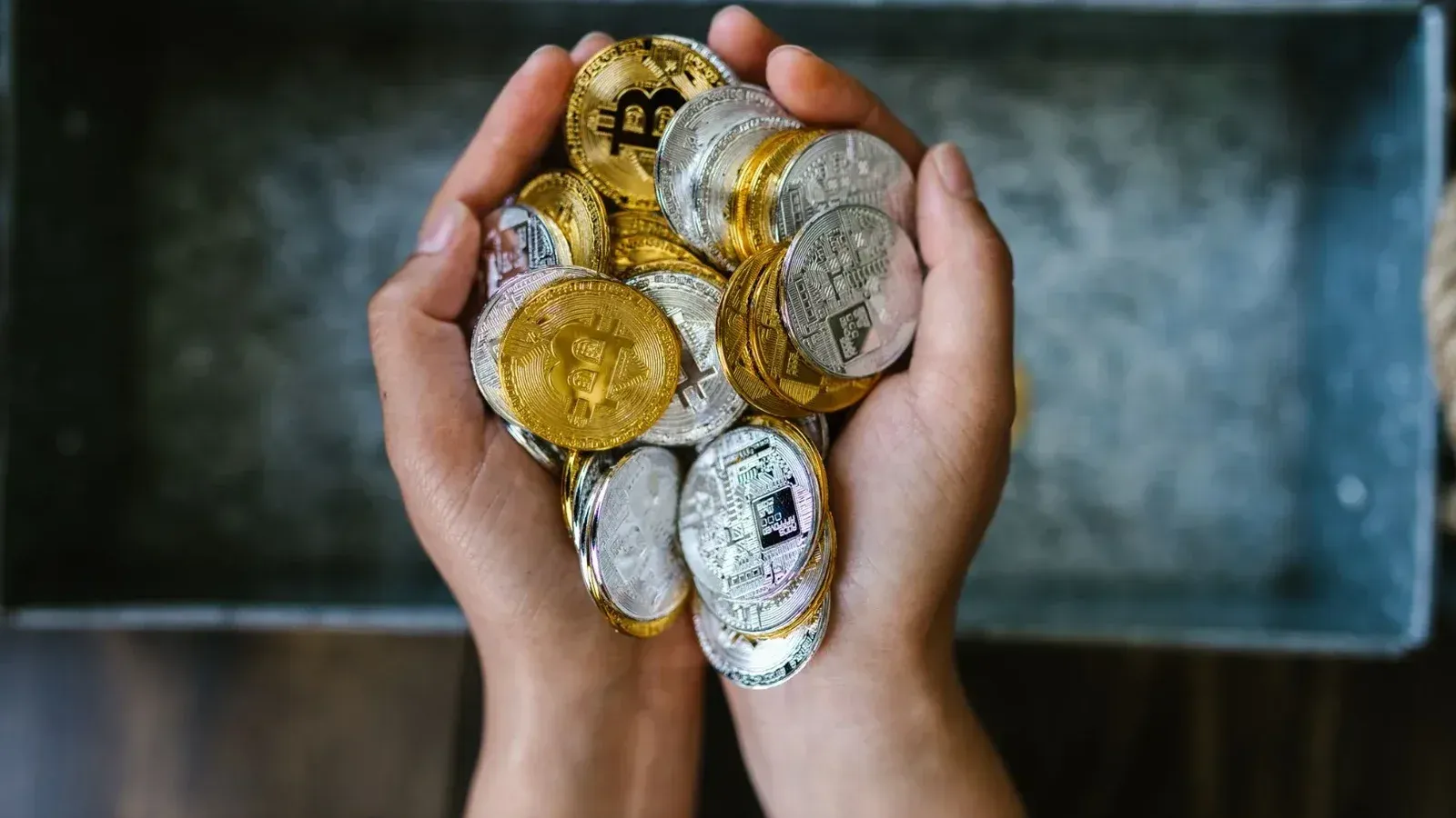 Close-up de manos sosteniendo monedas de criptomonedas de oro y plata, simbolizando la inversión digital.