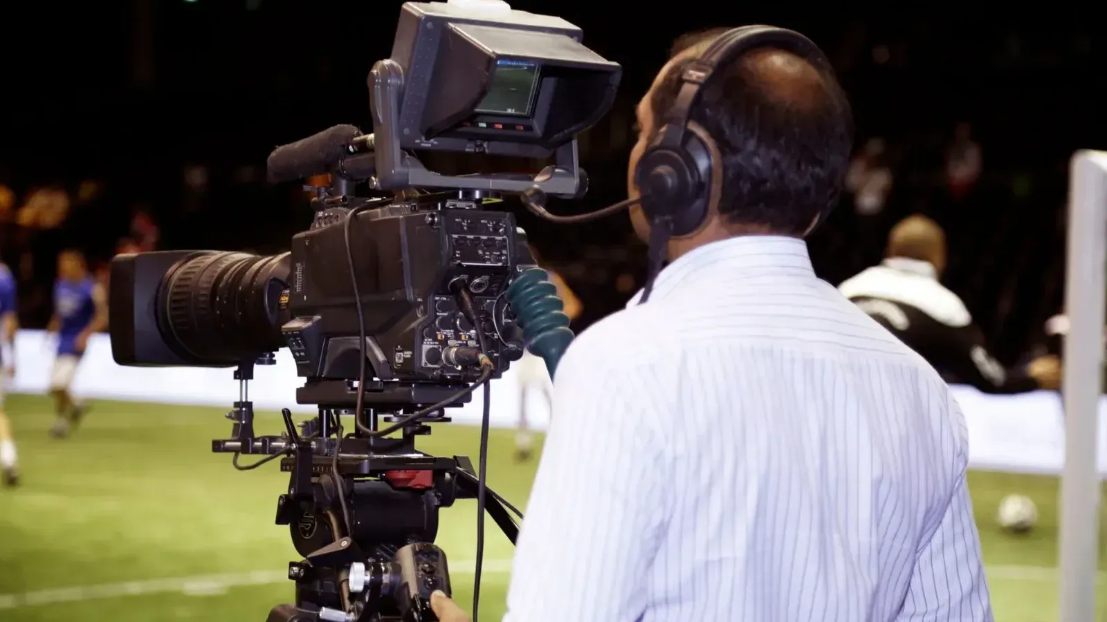 Un camarógrafo filmando un partido de fútbol en un estadio, capturando la acción en video.